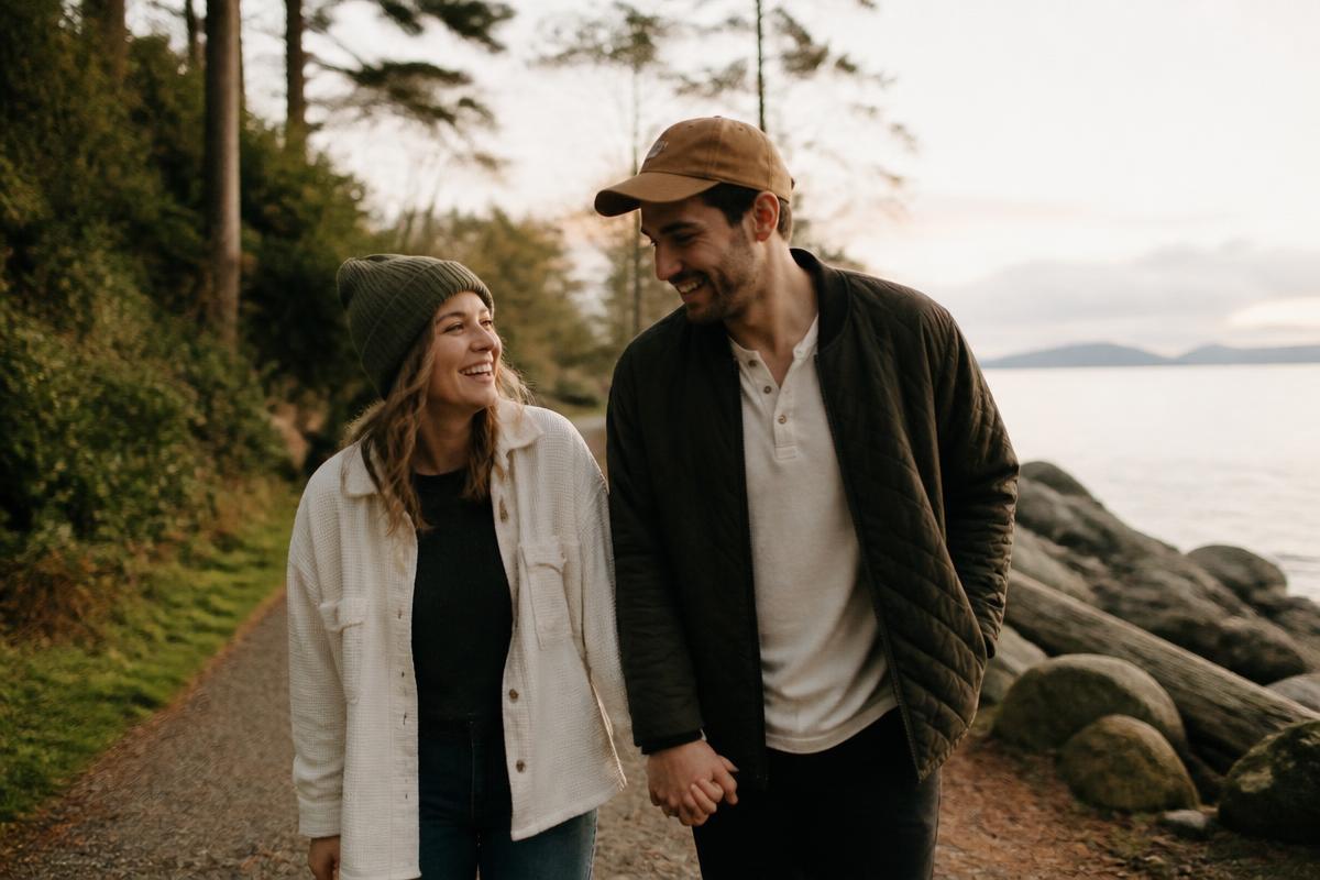 An engaged couple walking hand in hand along a coastal path at golden hour, laughing together